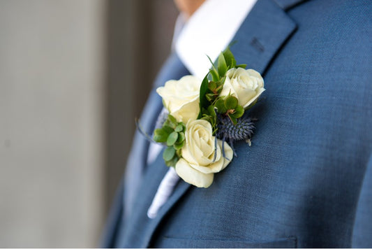 A white spray rose boutonniere is accented with blue thistles on a groom's medium blue suit.